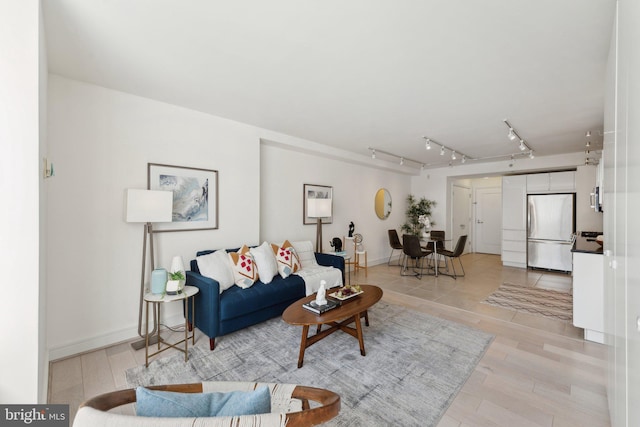 living area featuring track lighting, baseboards, and light wood-style floors