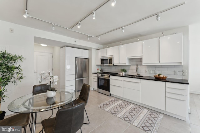 kitchen with tasteful backsplash, rail lighting, stainless steel appliances, white cabinetry, and a sink