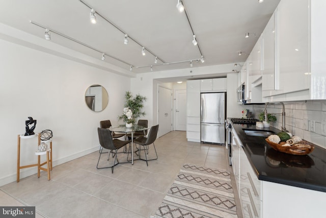 kitchen with a sink, stainless steel appliances, white cabinets, dark countertops, and tasteful backsplash