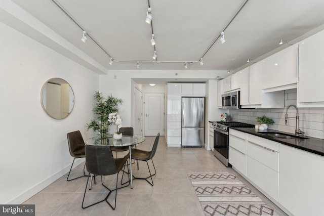 kitchen featuring tasteful backsplash, appliances with stainless steel finishes, rail lighting, white cabinets, and a sink