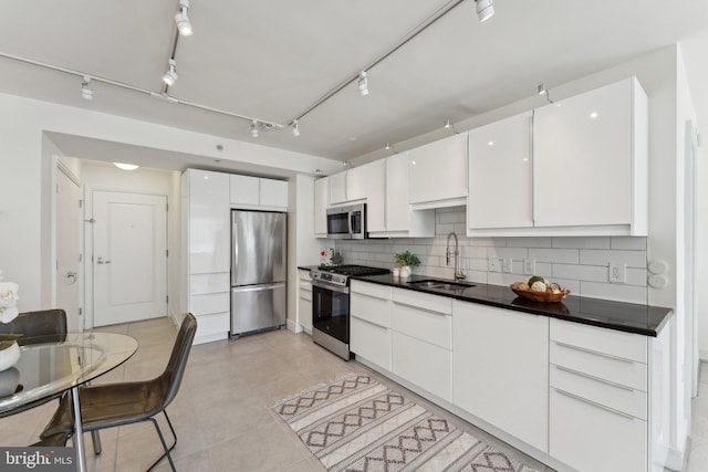 kitchen with dark countertops, decorative backsplash, white cabinets, stainless steel appliances, and a sink