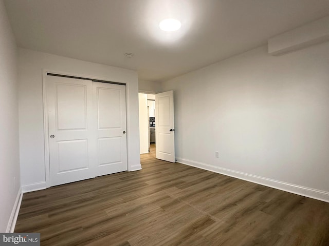 unfurnished bedroom with dark wood-style floors, a closet, and baseboards