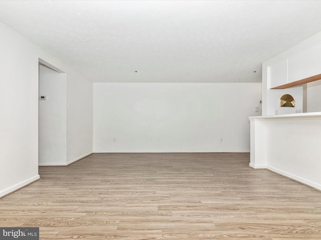 spare room featuring light wood-type flooring, baseboards, and a textured ceiling