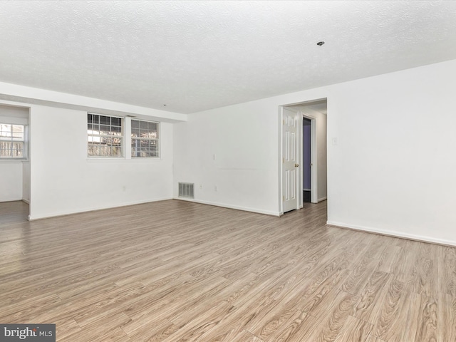 empty room with light wood-style flooring, baseboards, visible vents, and a textured ceiling