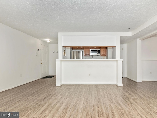 unfurnished living room featuring light wood-style flooring, a textured ceiling, and baseboards