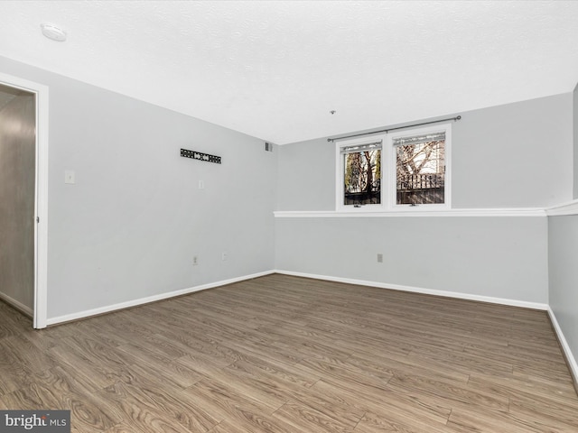 spare room with visible vents, a textured ceiling, baseboards, and wood finished floors