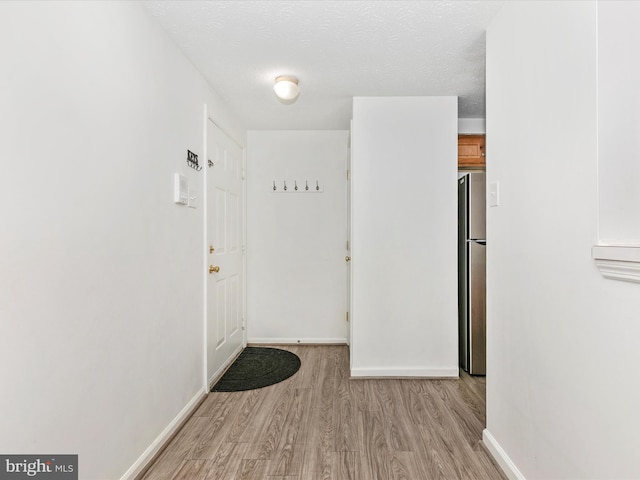 doorway featuring light wood-style floors, baseboards, and a textured ceiling