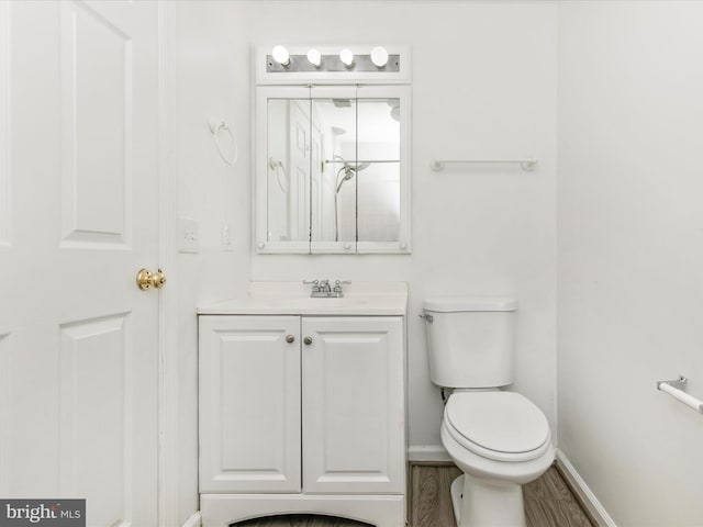 bathroom featuring baseboards, toilet, wood finished floors, and vanity