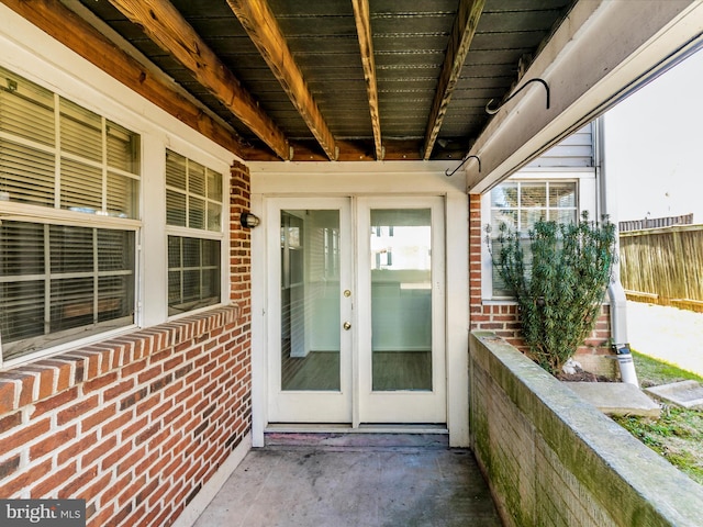 view of exterior entry featuring french doors, brick siding, and fence