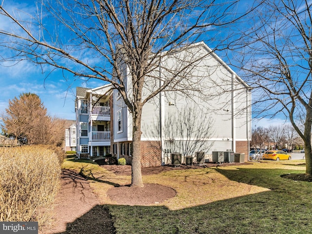 view of side of property featuring a balcony, a yard, central AC unit, and brick siding