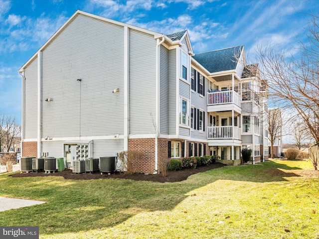 view of home's exterior with a lawn, central AC unit, a balcony, and brick siding