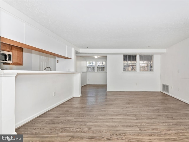 unfurnished living room featuring visible vents, a textured ceiling, light wood-type flooring, and baseboards