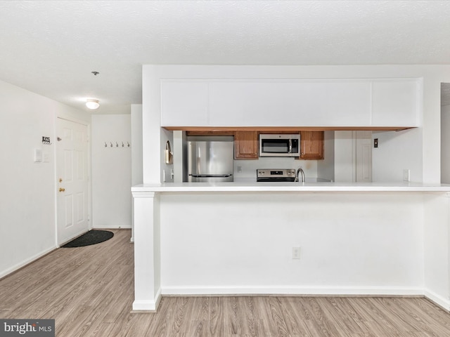 kitchen featuring light wood finished floors, appliances with stainless steel finishes, a textured ceiling, and light countertops