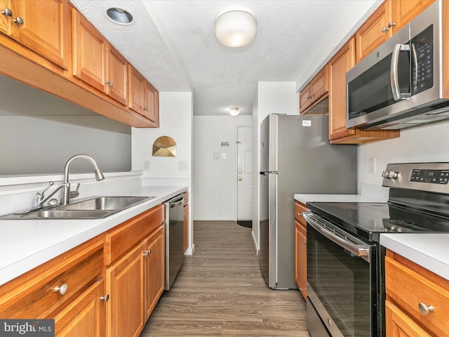 kitchen with brown cabinets, a sink, stainless steel appliances, light wood finished floors, and light countertops