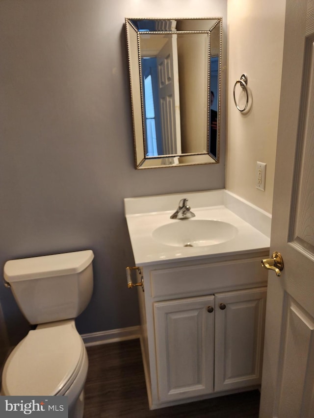 half bathroom with toilet, vanity, baseboards, and wood finished floors
