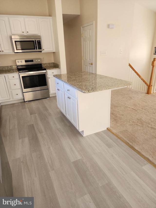 kitchen featuring light wood finished floors, white cabinets, stainless steel appliances, and light stone countertops