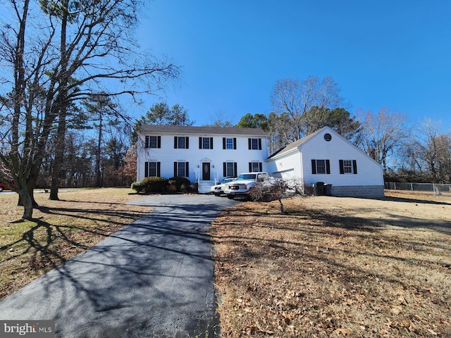 colonial inspired home with aphalt driveway, fence, and a front lawn