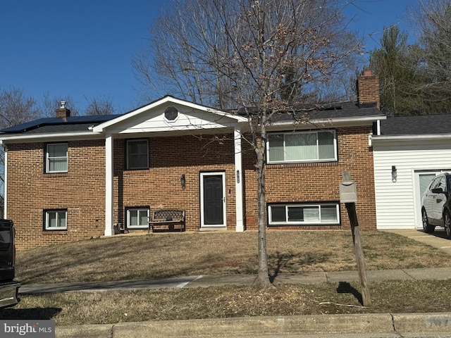 split foyer home featuring roof mounted solar panels, brick siding, and a chimney