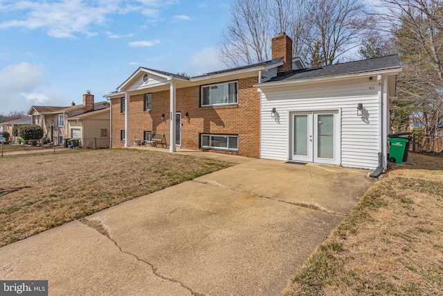 back of property with a patio, a chimney, french doors, a lawn, and brick siding