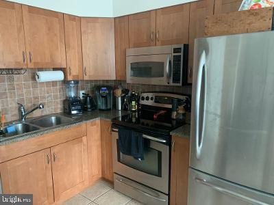 kitchen featuring brown cabinetry, appliances with stainless steel finishes, a sink, backsplash, and light tile patterned flooring