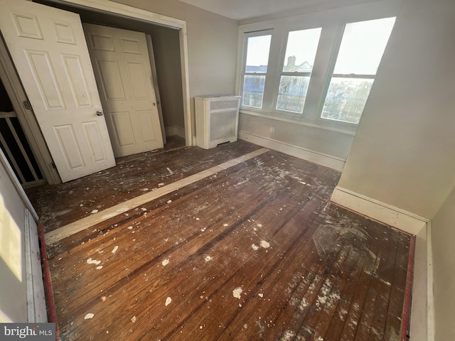 unfurnished bedroom with radiator heating unit, hardwood / wood-style floors, and baseboards