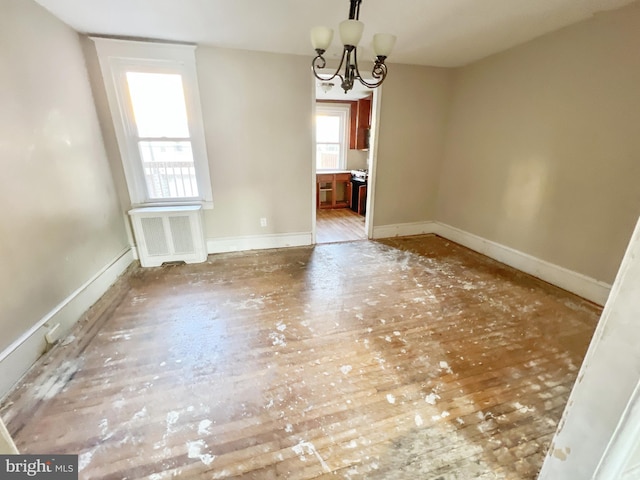 unfurnished dining area with baseboards, radiator, and an inviting chandelier