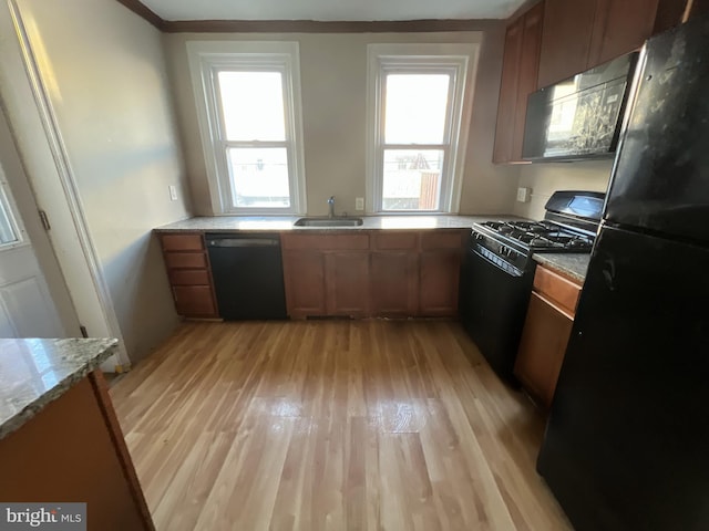 kitchen with black appliances, brown cabinets, a sink, and light wood-style floors