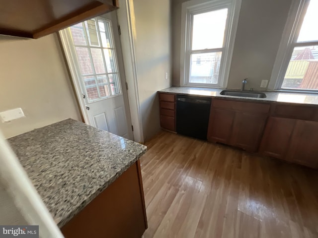 kitchen with brown cabinets, a sink, light stone countertops, light wood-type flooring, and dishwasher