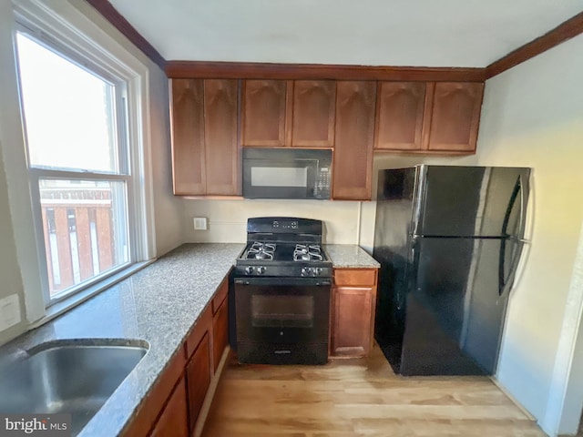 kitchen with light stone counters, a sink, light wood-type flooring, brown cabinets, and black appliances