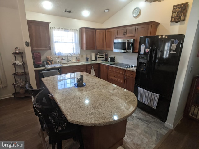 kitchen featuring a kitchen island, light stone counters, vaulted ceiling, black appliances, and a sink