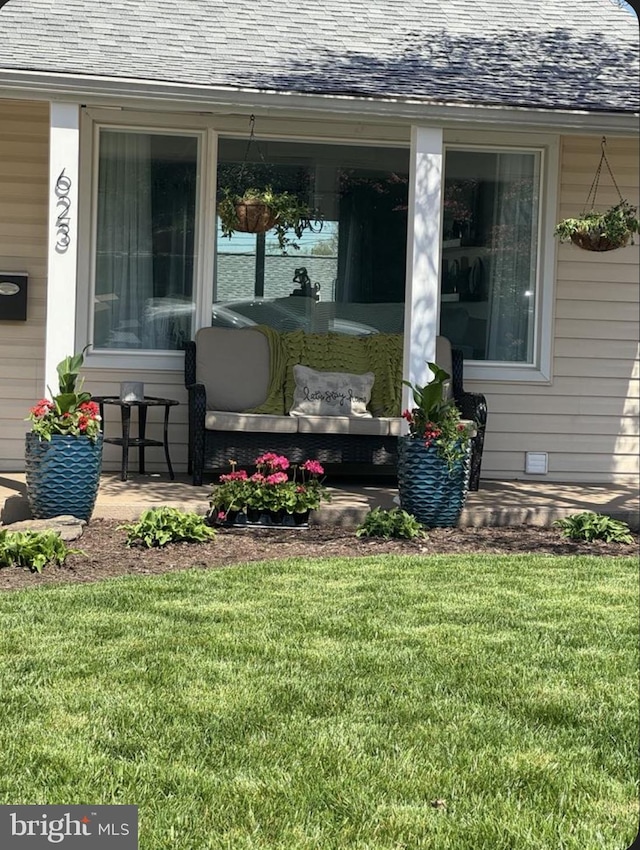 view of exterior entry with a porch, roof with shingles, and a yard