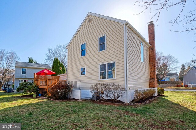 rear view of property with a deck, a lawn, and a chimney