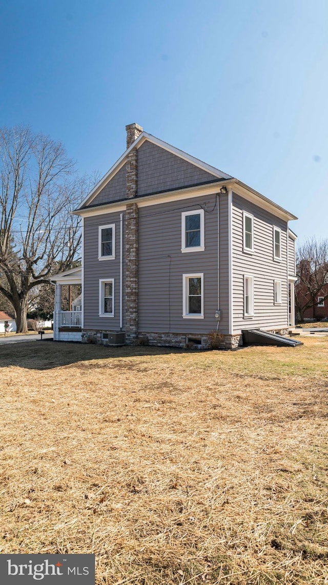 rear view of property featuring covered porch, a lawn, and a chimney