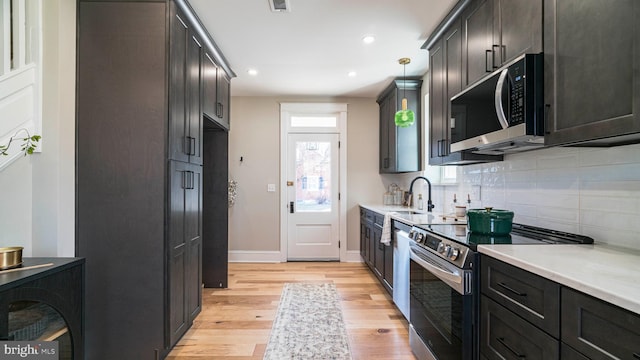 kitchen with light countertops, light wood-style flooring, decorative backsplash, appliances with stainless steel finishes, and a sink