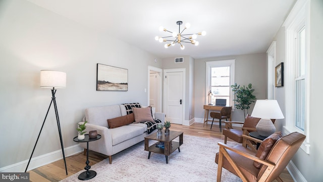 living area featuring baseboards, light wood-type flooring, visible vents, and a notable chandelier