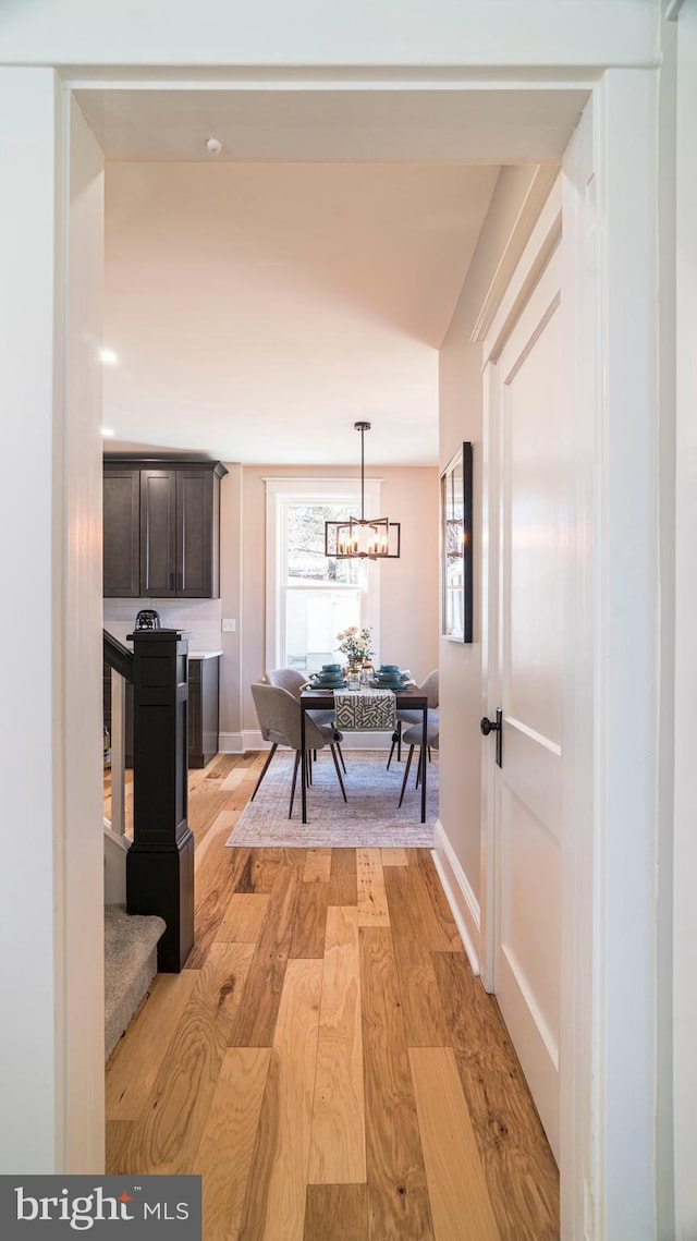 corridor with light wood-style floors, baseboards, and an inviting chandelier