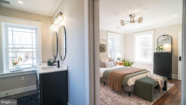 bedroom with wood finished floors, a sink, visible vents, baseboards, and ornamental molding