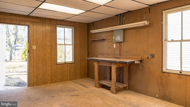 basement with a paneled ceiling, electric panel, and a healthy amount of sunlight