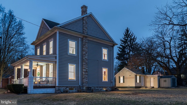 view of home's exterior featuring an outbuilding, covered porch, a storage shed, a lawn, and a chimney