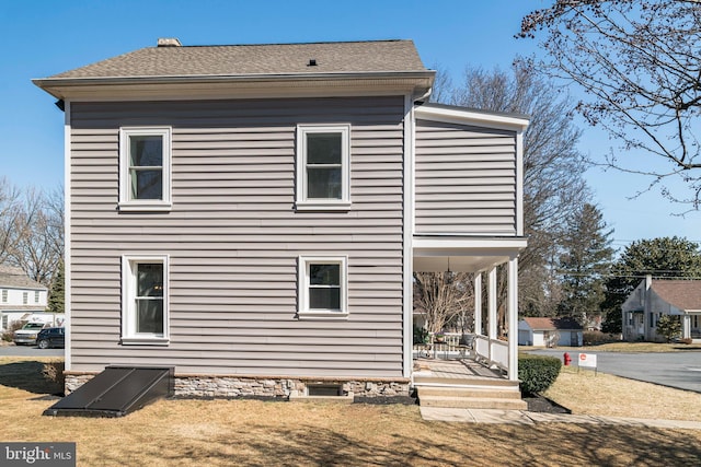 back of property with a shingled roof, a porch, and a lawn