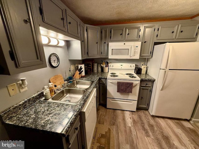 kitchen with a textured ceiling, white appliances, a sink, light wood-style floors, and dark countertops