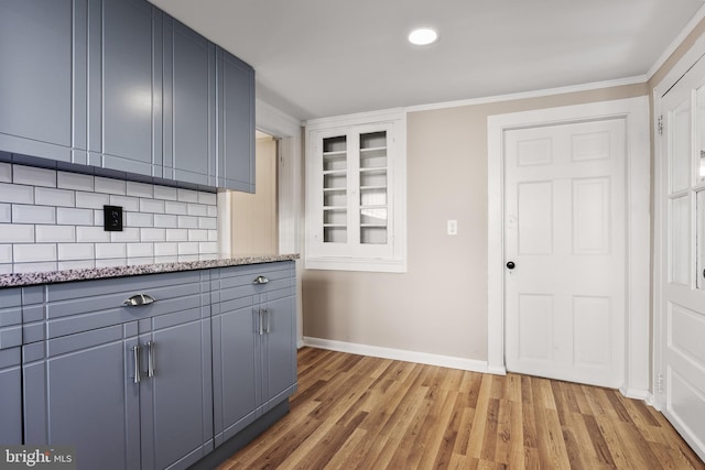 kitchen with baseboards, ornamental molding, light stone countertops, gray cabinetry, and light wood-type flooring