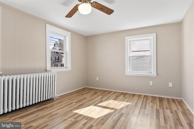 unfurnished room featuring radiator, a wealth of natural light, a ceiling fan, and wood finished floors