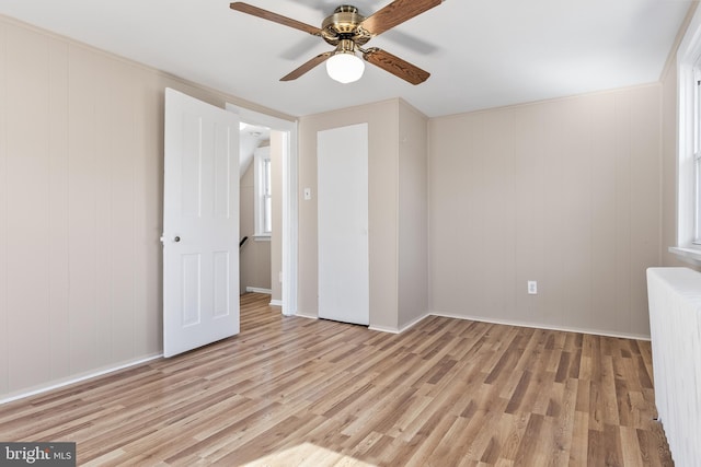 empty room with baseboards, light wood-type flooring, a ceiling fan, and radiator