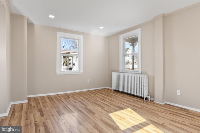 empty room with radiator, light wood-style floors, plenty of natural light, and baseboards