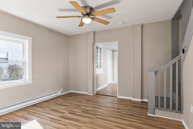 spare room with a baseboard heating unit, wood finished floors, a ceiling fan, baseboards, and stairs