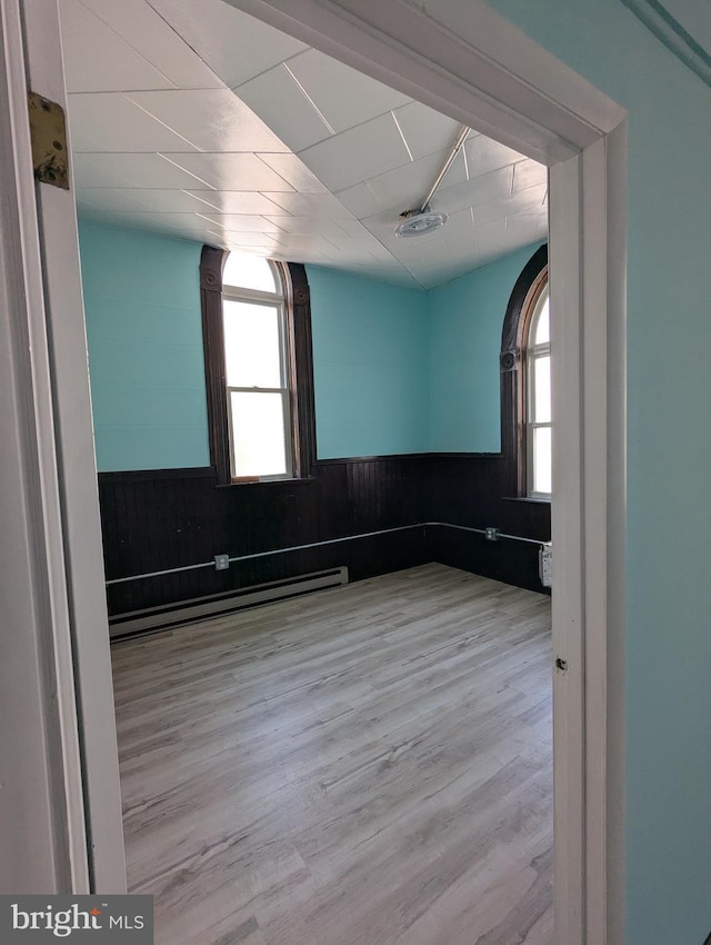 unfurnished room featuring a wainscoted wall, plenty of natural light, a baseboard heating unit, and wood finished floors