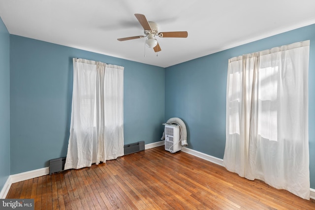 empty room featuring a baseboard heating unit, a ceiling fan, baseboards, and wood-type flooring