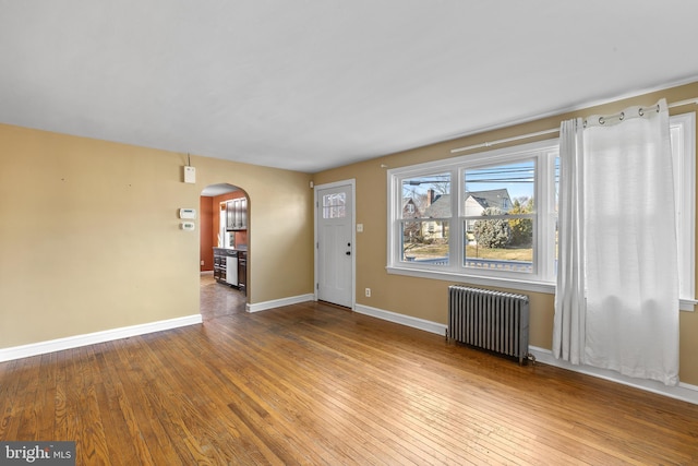 entryway featuring arched walkways, radiator heating unit, baseboards, and hardwood / wood-style flooring