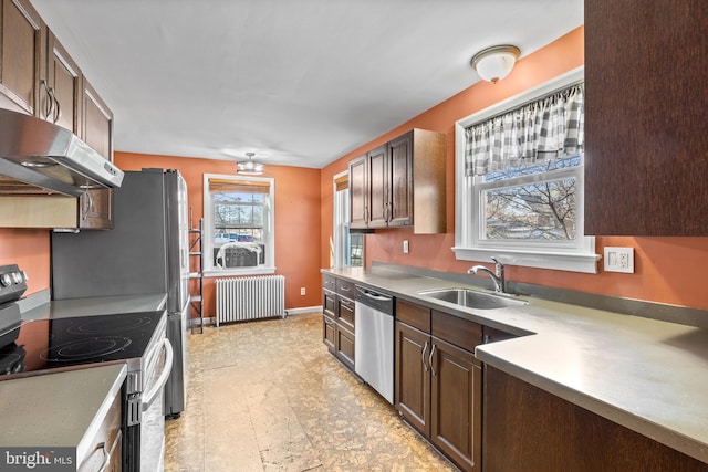 kitchen with baseboards, under cabinet range hood, radiator heating unit, stainless steel appliances, and a sink